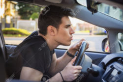 File of Young Man Driving Car and Leaning Forward and Peering Through Car Windshield Stock Photo